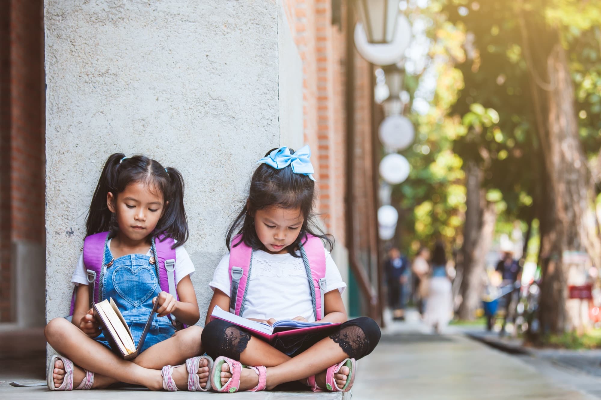 Two school-age girls read and write together outdoors.